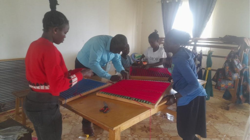 Kujenga Inclusive Game Changing School-A student's hands carefully manipulating threads on an adaptive loom, mastering the weaving craft